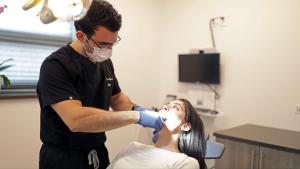 Image of Dr.Lee Kojanis from Premier Oral examining a patient wearing a black scrub, a mask, and gloves.