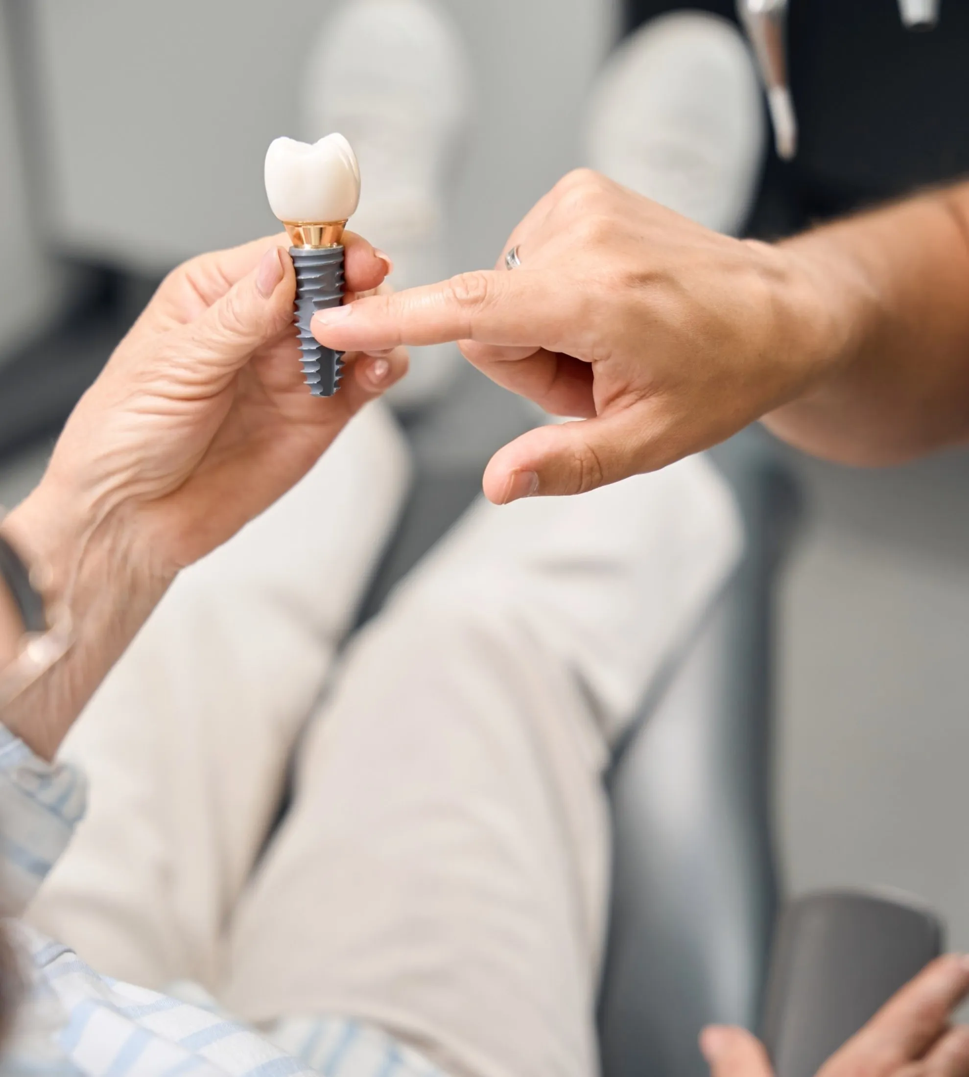 Patient examining a dental implant model with a crown, illustrating root-level bone support and restoration.