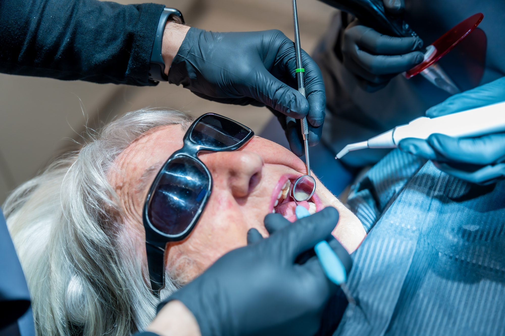Oral surgeon performing a dental procedure on a senior patient wearing protective glasses in a clinical setting.
