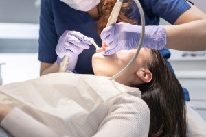 Oral surgeon performing a dental procedure with instruments while the patient reclines comfortably.
