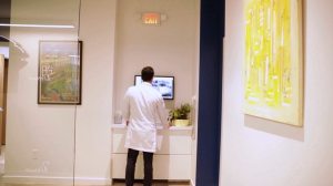 Oral surgeon in a white coat reviewing scans on a screen in Premier Oral Surgery Group’s hallway.