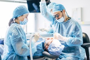Oral surgeons performing a procedure using sterile instruments while treating a patient in a modern dental clinic.