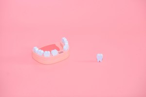A wooden jaw model illustrating the impact of a single missing tooth placed on a plain background.