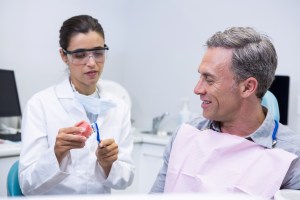 Dentist explains a procedure to a smiling patient using a small model at Premier Oral and Maxillofacial Surgery Group.