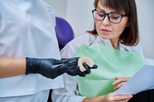 Premier Oral and Maxillofacial Surgery group specialist shows a jaw model to a female patient in glasses.