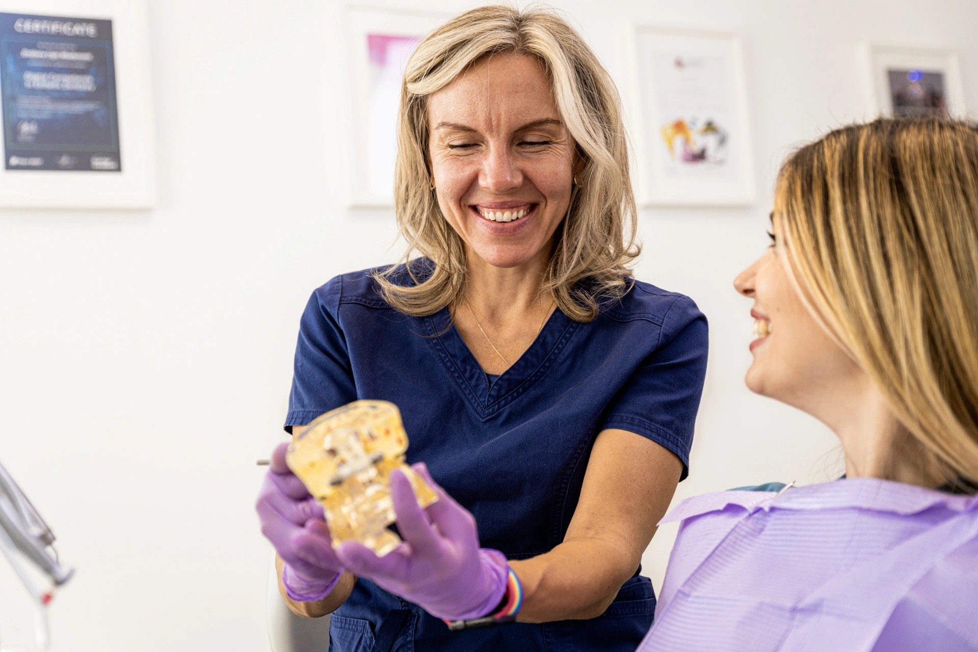 Premier oral surgery and maxillofacial group’s surgeon smiling and showing a dental jaw model to a patient.